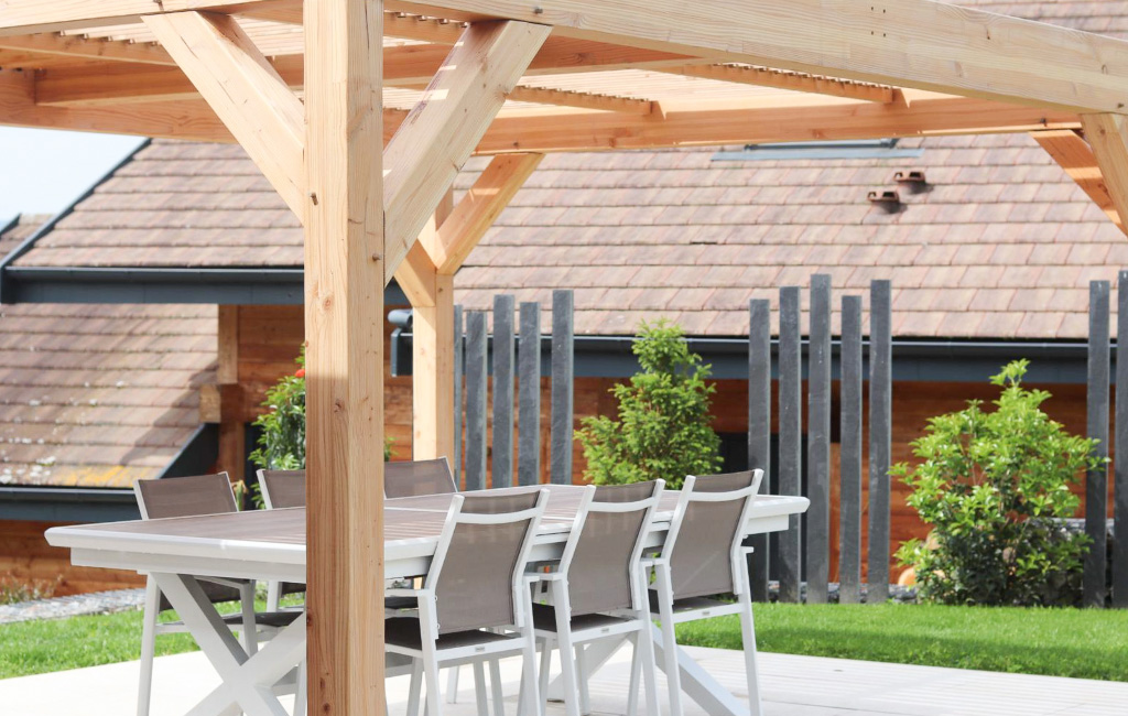 pergola-bois-id jardins Pergola en bois posée sur une terrasse, créant un espace ombragé dans un jardin aménagé par ID Jardins.
